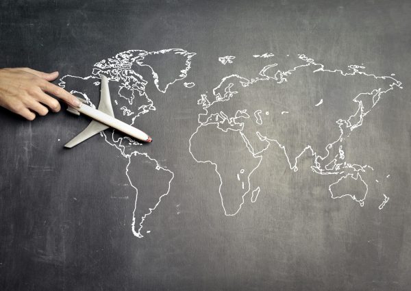 From above of crop anonymous person driving toy airplane on empty world map drawn on blackboard representing travel concept