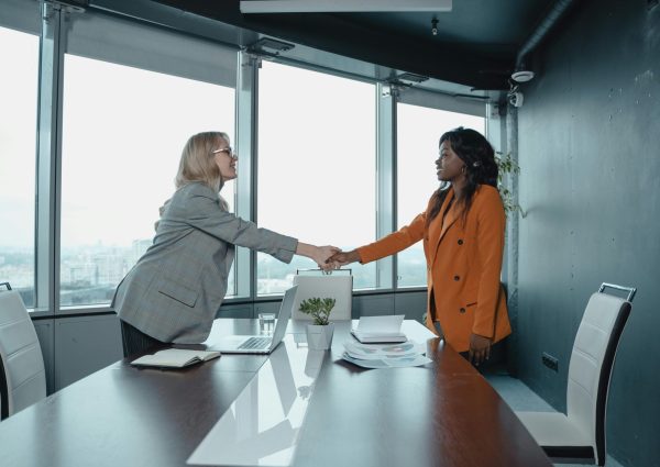Two businesswomen shaking hands in a modern office setting, symbolizing partnership and agreement.